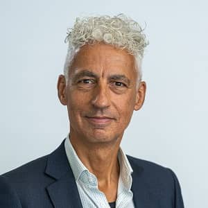 Man met grijs krulletjeshaar en een blauwe blazer in de hal van het ministerie van OCW. Dit is Sal Stam.